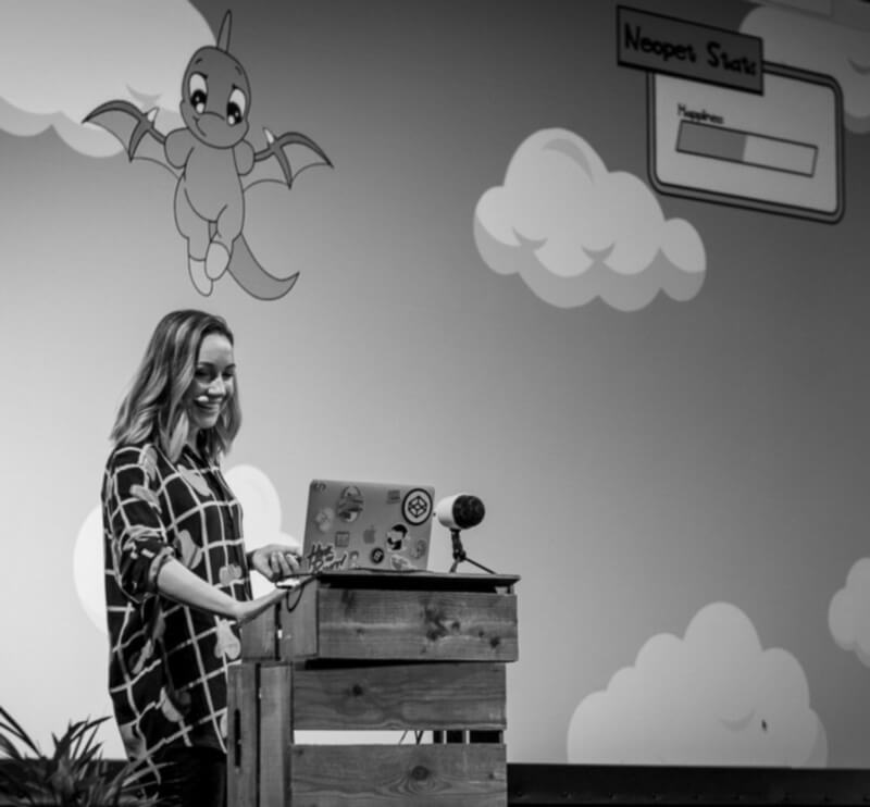 black and white photo of Megha on stage at beyond tellerrand. Screen behind her shows an SVG neopet.